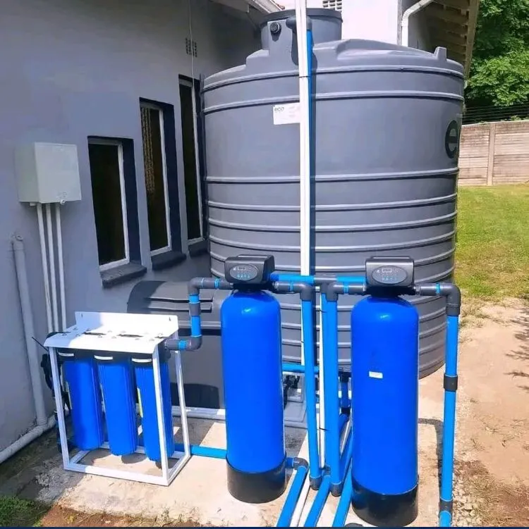 Two blue filter vessels and a three-stage filter connected to a large tank beside a house