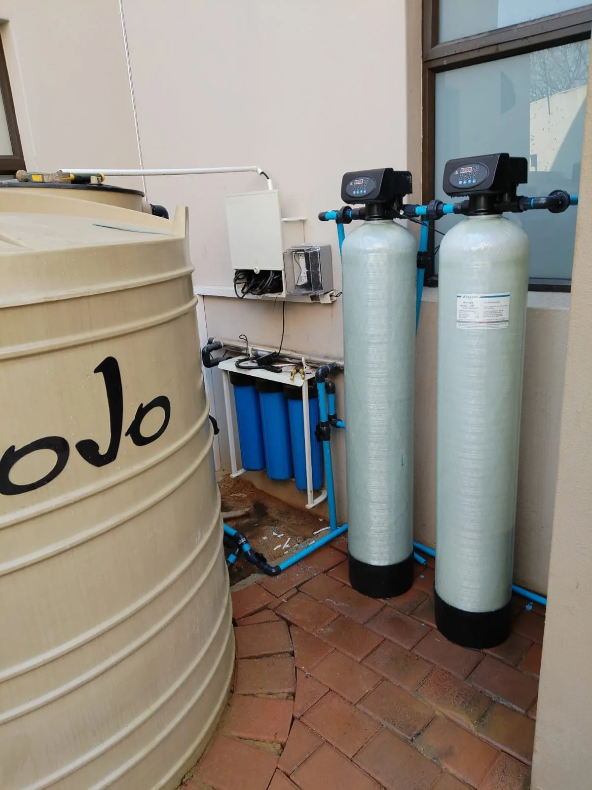 Two tall filter vessels next to a tank and filter housing in a paved courtyard
